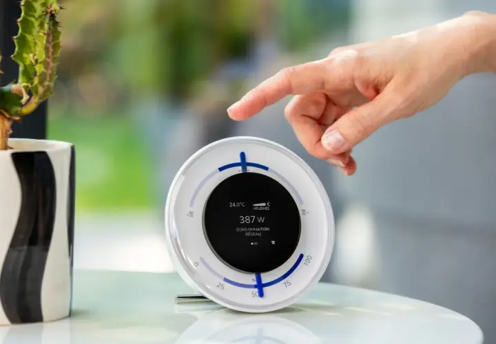 Un doigt effleure un écran affichant "387 W CONSOMMATION RÉSEAU", utile pour comment suivre sa production photovoltaïque EDF.