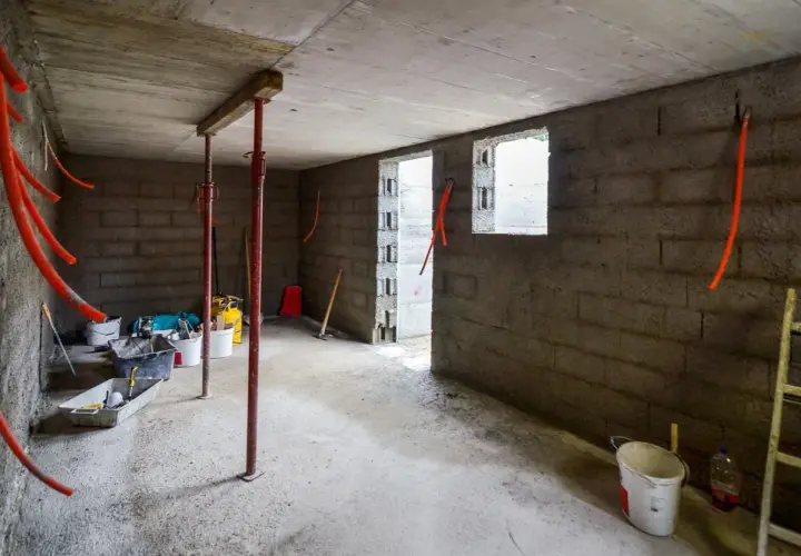 Intérieur brut d'une cave en construction, avec des tuyaux orange, des seaux et des étais. L'isolation de cette cave est en cours.