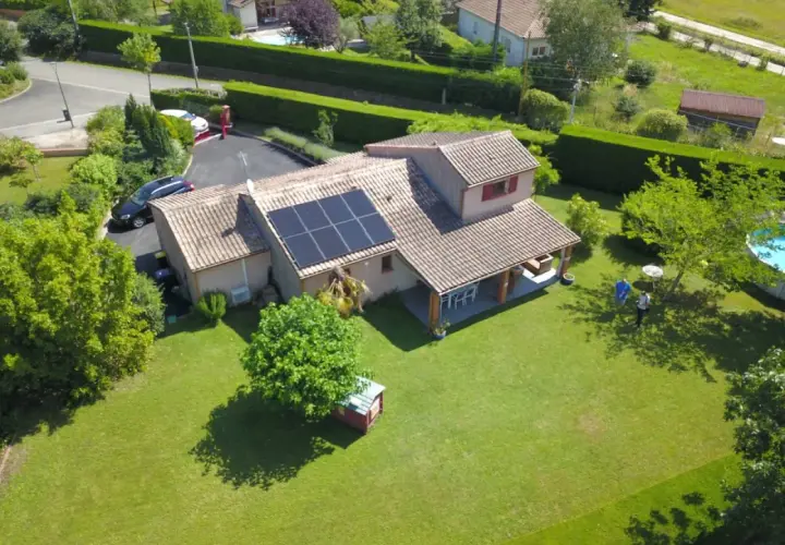 Maison avec panneaux photovoltaïques sur le toit, jardin verdoyant, piscine et deux personnes discutant.