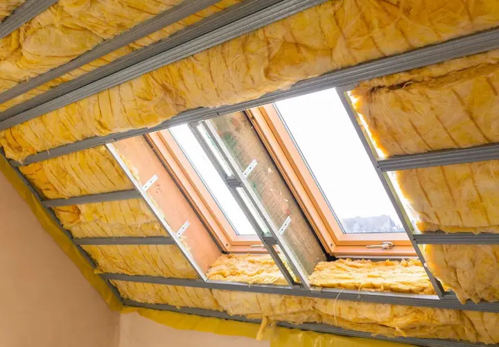 Isolation des combles aménageables avec laine de verre jaune sous une structure métallique. Des fenêtres de toit laissent passer la lumière.