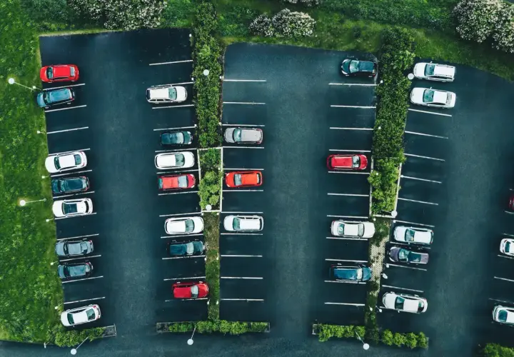 Vue aérienne d'un parking avec des voitures garées. La loi aper est respectée, avec des places bien délimitées et des espaces verts.
