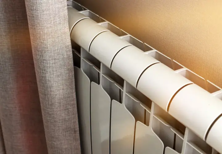 Radiateur blanc près d'un rideau gris. Le fluide caloporteur circule pour chauffer la pièce.