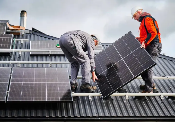 Deux techniciens travaillent sur une toiture pour l'installation de panneaux solaires. L'un tient un panneau, l'autre est penché.
