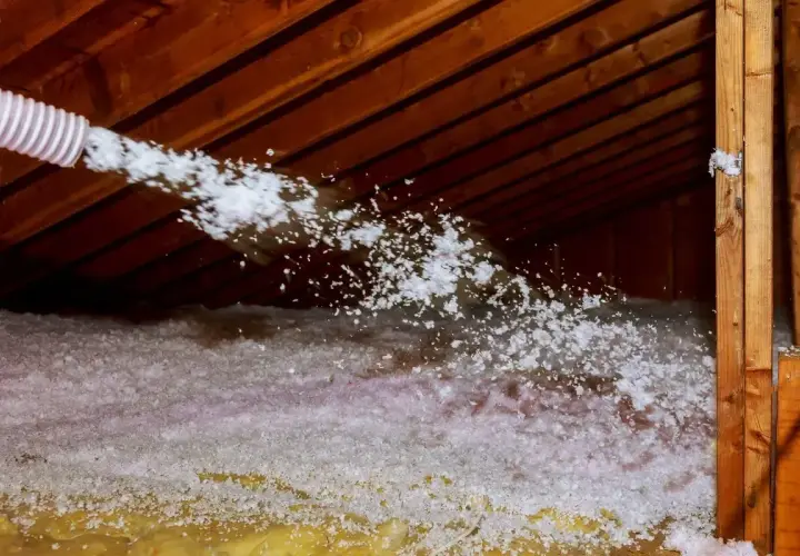 Un tuyau souffle de l'isolant dans un grenier. Attention au sel de bore, un danger potentiel pour la santé.
