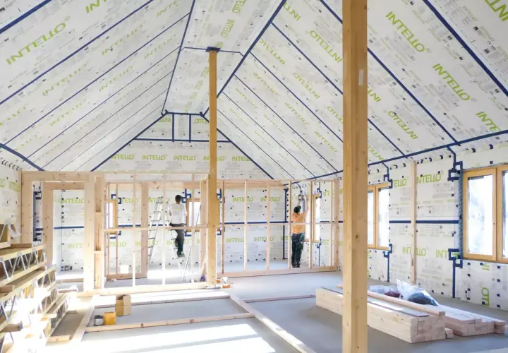 Construction d'une maison avec membrane d'étanchéité à l'air obligatoire. Des ouvriers installent la membrane sur les murs et le toit.