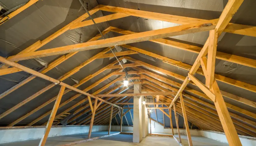 Charpente en bois d'un grenier en cours d'aménagement, avec une bâche noire recouvrant la structure de la r toiture.