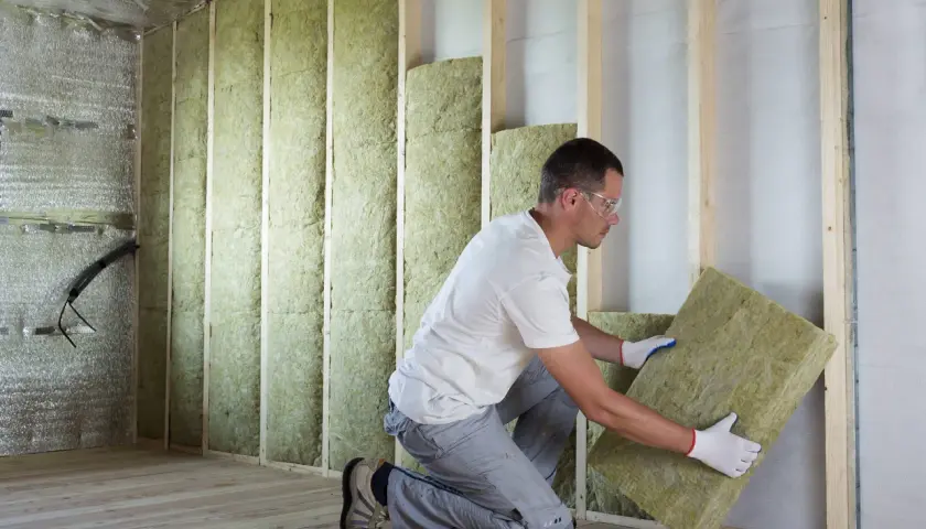 Pose d'isolant minéral pour respecter la norme isolation thermique rénovation. Un ouvrier installe des panneaux dans une structure en bois.