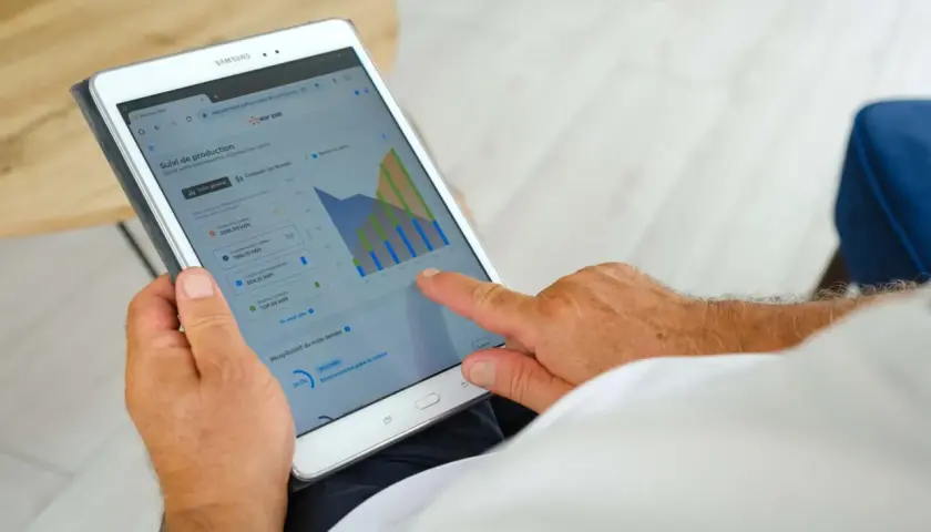 Un homme consulte sur sa tablette le suivi de sa production solaire EDF ENR, vérifiant le délai signature contrat EDF OA.