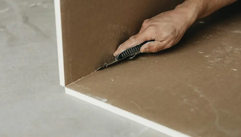 Main d'un artisan coupant une plaque de Fermacell ou de Placo avec un cutter. Travaux de rénovation en cours.