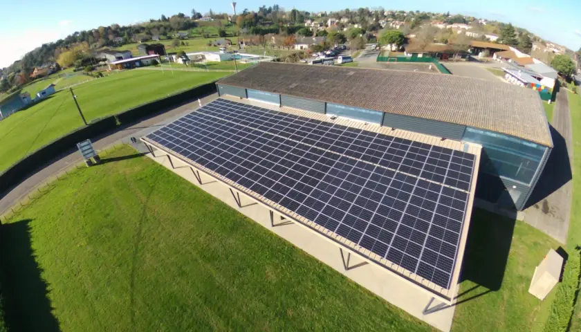 Panneaux solaires sur un bâtiment, assurant une rentabilité 100 kw photovoltaïque. Le paysage environnant est verdoyant.