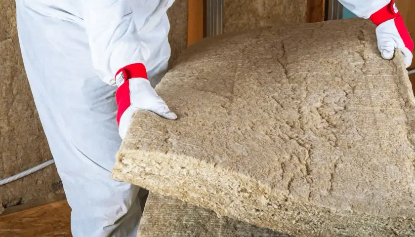 Un ouvrier en combinaison blanche manipule un panneau de laine de bois soufflée, prêt à isoler une maison.