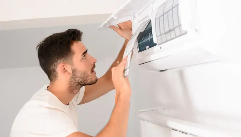 Un homme nettoie la climatisation de sa maison, retirant le filtre pour un entretien.