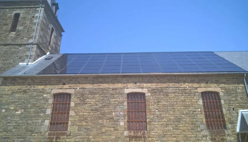 Panneaux solaires installés sur le toit d'un bâtiment en pierre, possiblement dans une zone classée, sous un ciel bleu clair.