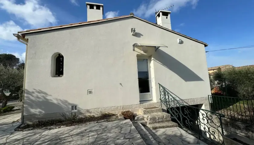 Maison Phénix 1970, blanche, avec cheminées, sous un ciel bleu. Escalier en pierre menant à la porte.