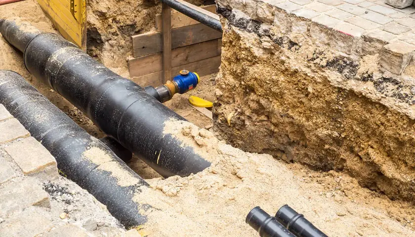 Gros tuyaux noirs enfouis dans le sable, prêts pour le chauffage urbain. Des travaux de voirie en cours.