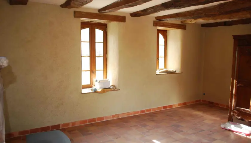 Murs en chaux chanvre pour une isolation naturelle et saine. Plancher de terre cuite et poutres apparentes dans une pièce lumineuse.