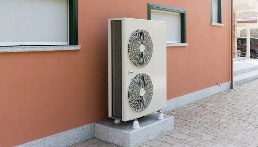 Unité extérieure d'une pompe à chaleur géothermique, installée sur un socle devant un mur ocre. Le prix de ce système est un investissement pour le confort.