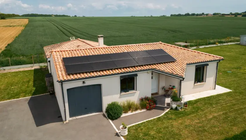 Maison avec toiture photovoltaïque, entourée de verdure et de champs.