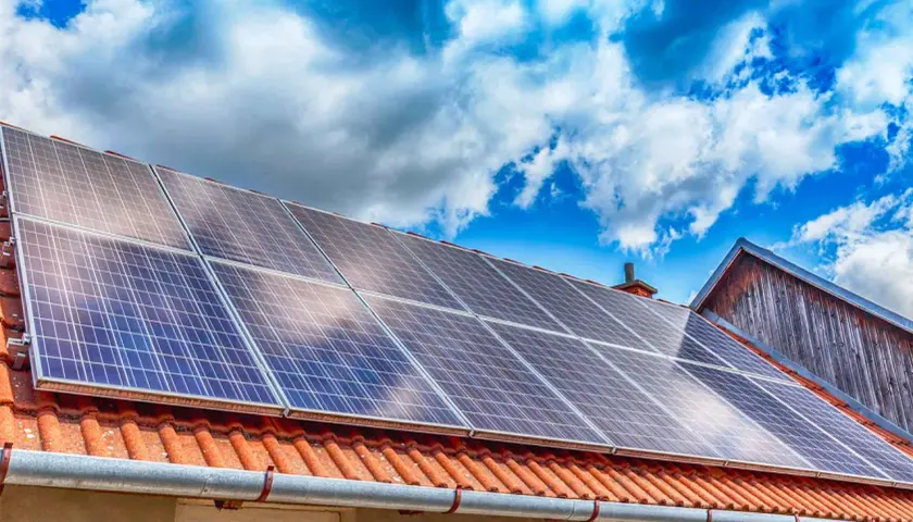 Panneaux solaires sur un toit de tuiles rouges, sous un ciel bleu et nuageux. Une installation qui assure une garantie pour l'avenir.