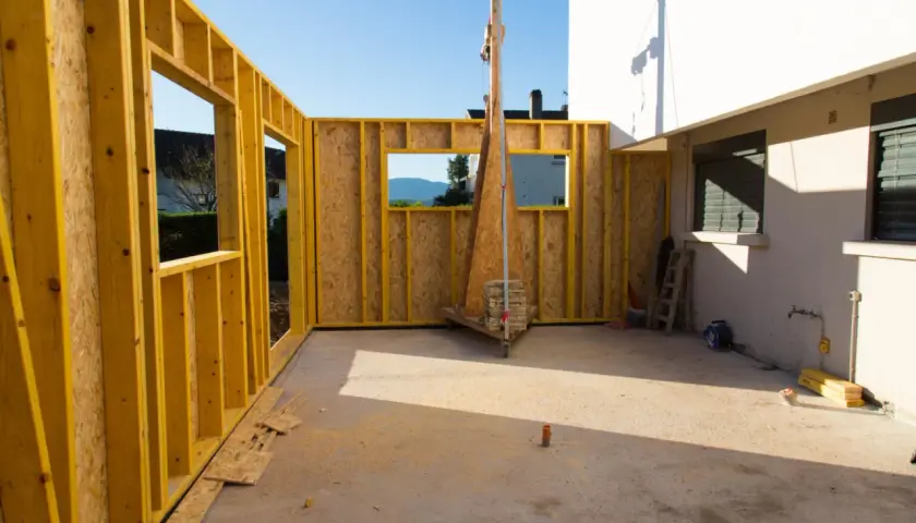 Chantier d'une extension bois, murs en ossature jaune et panneaux OSB, avec vue sur le paysage.