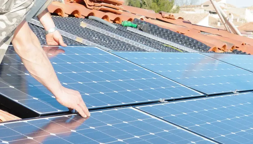 Installation de panneaux solaires sur un toit. Une main ajuste un panneau, préparant la revente du surplus photovoltaïque sans RGE.