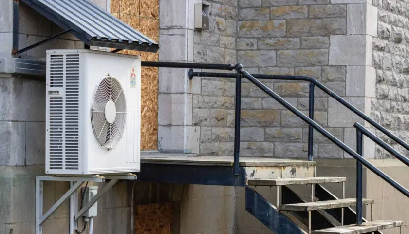 Unité extérieure de climatisation sous un auvent, près d'un escalier en métal et en bois. Idéal pour savoir où placer sonde température extérieure.