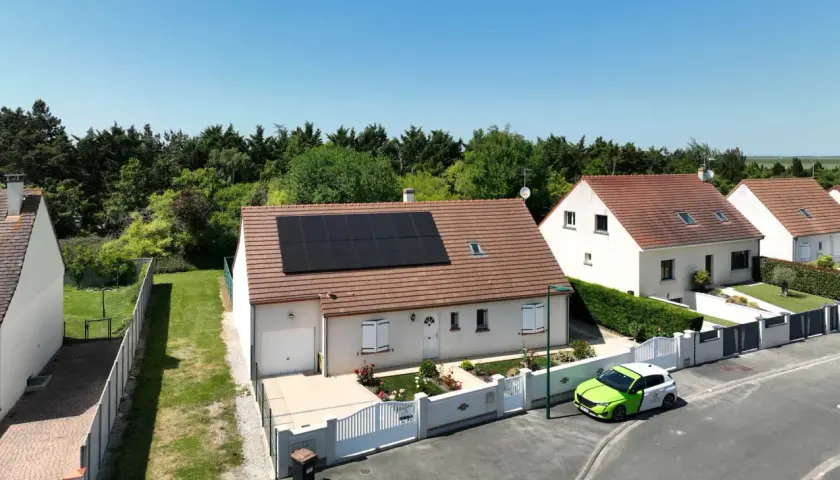Maison avec panneaux photovoltaïques en vente, un véhicule vert et blanc garé devant.