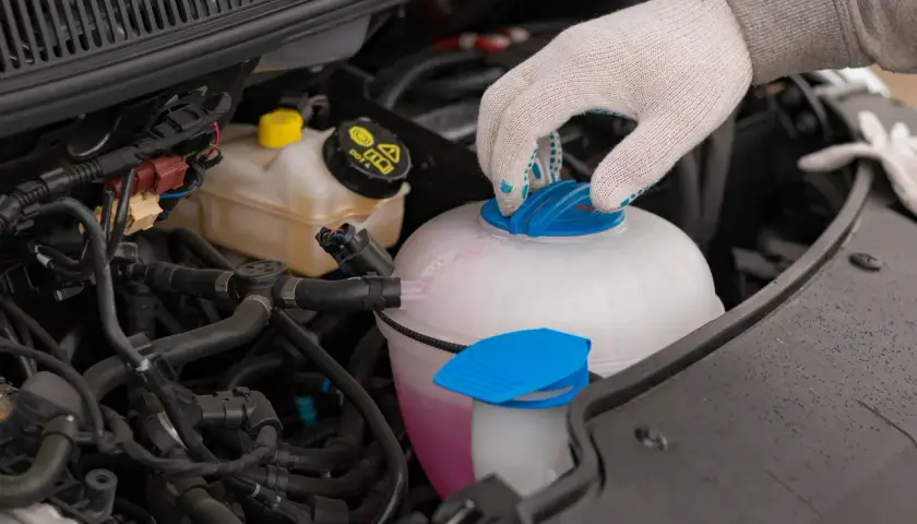 Main d'une personne portant un gant blanc ferme le bouchon d'un vase d'expansion rempli d'eau et de liquide de refroidissement rose.