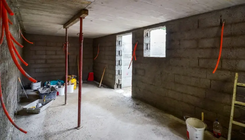 Intérieur brut d'une cave en construction, avec des tuyaux orange, des seaux et des étais. L'isolation de cette cave est en cours.