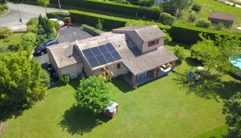 Maison avec panneaux photovoltaïques sur le toit, jardin verdoyant, piscine et deux personnes discutant.
