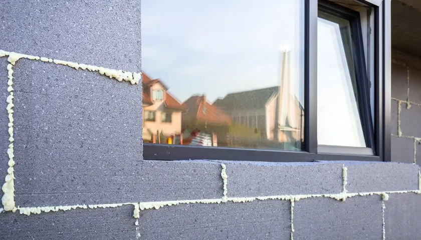 Mousse isolante appliquée sur des blocs de béton pour un enduit isolant extérieur. Reflets de maisons dans la fenêtre.