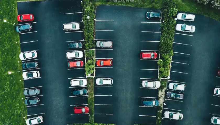Vue aérienne d'un parking avec des voitures garées. La loi aper est respectée, avec des places bien délimitées et des espaces verts.