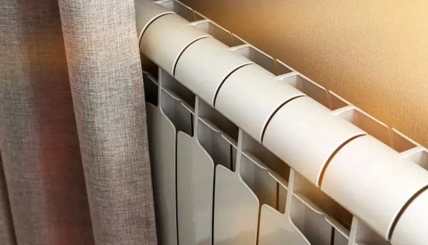 Radiateur blanc près d'un rideau gris. Le fluide caloporteur circule pour chauffer la pièce.