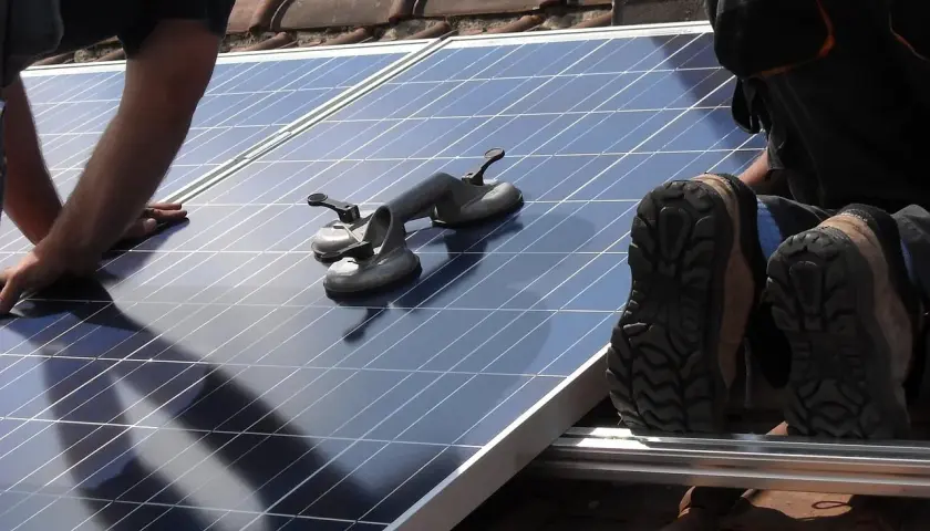 Un installateur panneau solaire agréé manipule un panneau sur un toit. Des ventouses sont prêtes à aider.