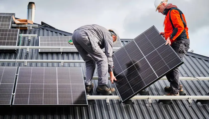 Deux techniciens travaillent sur une toiture pour l'installation de panneaux solaires. L'un tient un panneau, l'autre est penché.