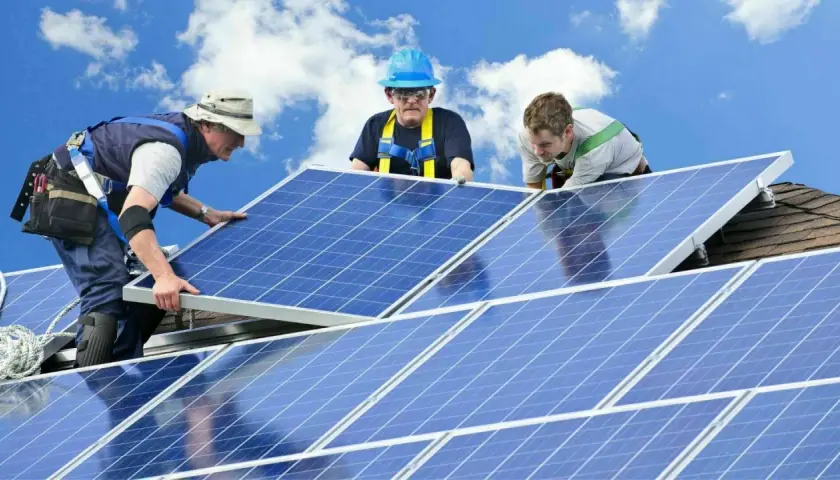 Trois techniciens installent des panneaux solaires sur un toit. Une installation sûre et pérenne, gage d'une **assurance décennale photovoltaïque** fiable.