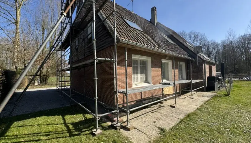 Échafaudage autour d'une maison en briques rouges, signe d'une rénovation maison de ville en cours. Le soleil brille sur le chantier.