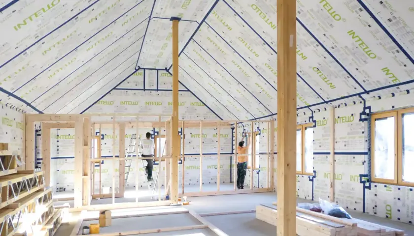 Construction d'une maison avec membrane d'étanchéité à l'air obligatoire. Des ouvriers installent la membrane sur les murs et le toit.
