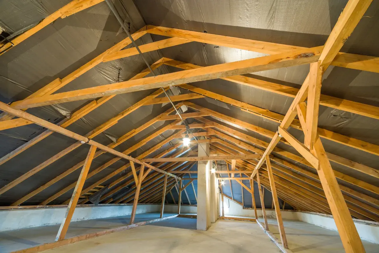 Charpente en bois d'un grenier en cours d'aménagement, avec une bâche noire recouvrant la structure de la r toiture.