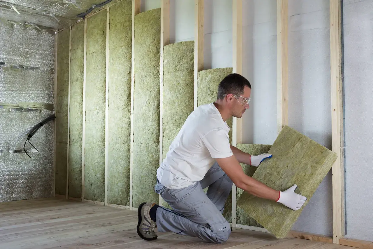 Pose d'isolant minéral pour respecter la norme isolation thermique rénovation. Un ouvrier installe des panneaux dans une structure en bois.