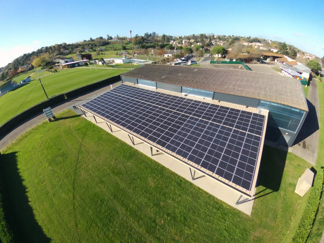 Panneaux solaires sur un bâtiment, assurant une rentabilité 100 kw photovoltaïque. Le paysage environnant est verdoyant.
