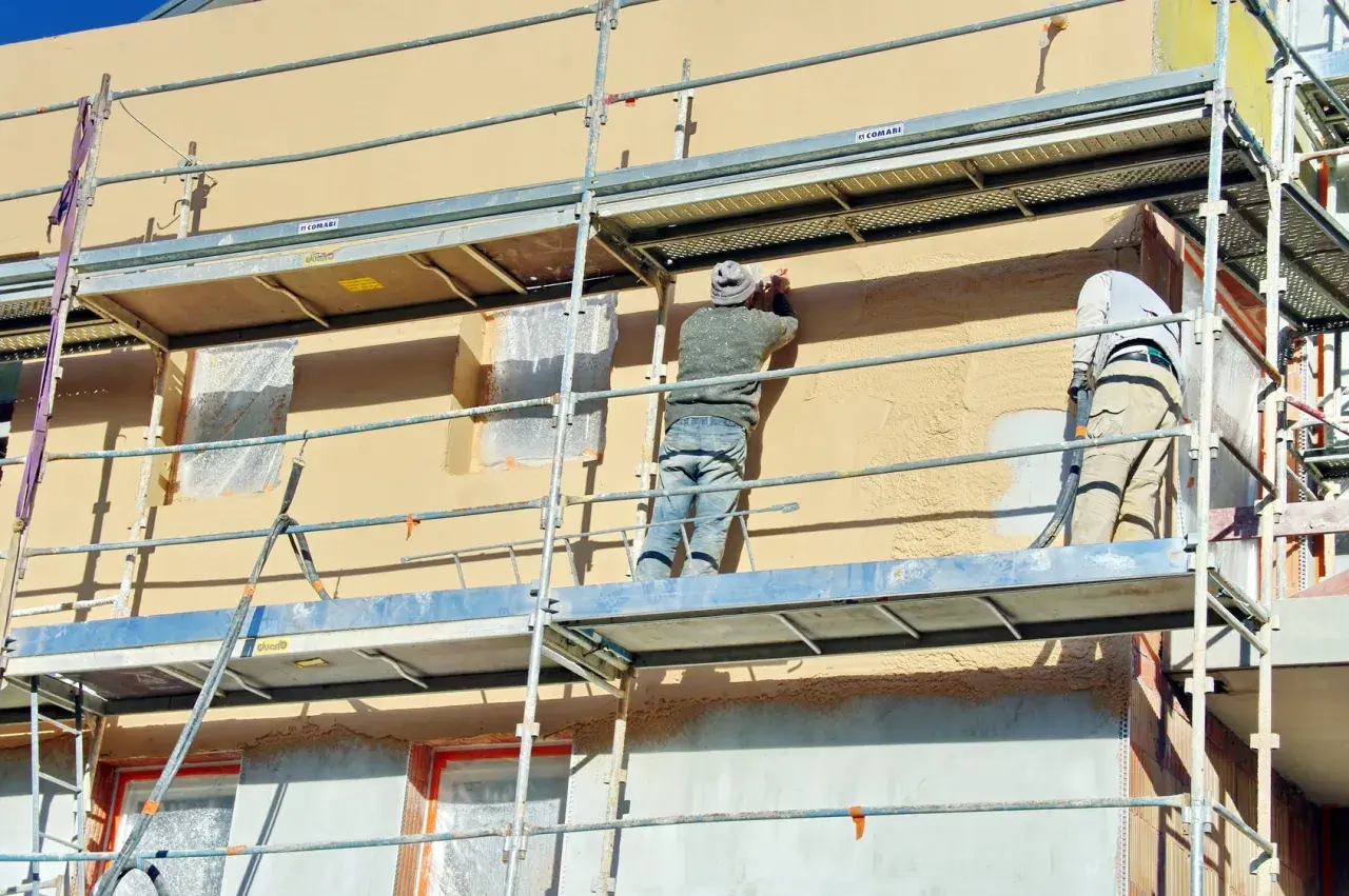 Travaux d'enduisage sur échafaudage. Le prix pour enduire un mur extérieur dépend de la technique et des matériaux.