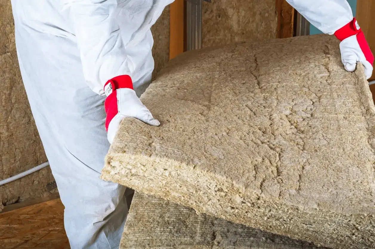 Un ouvrier en combinaison blanche manipule un panneau de laine de bois soufflée, prêt à isoler une maison.