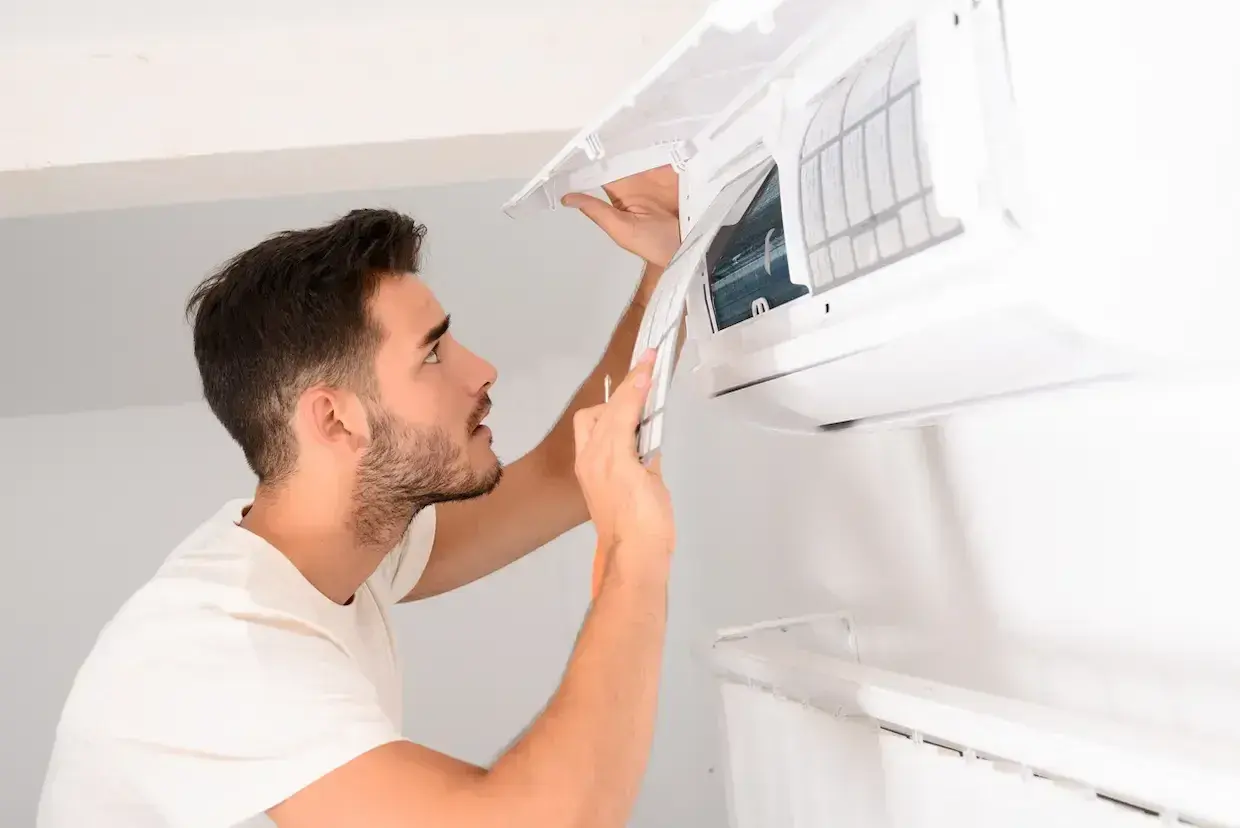 Un homme nettoie la climatisation de sa maison, retirant le filtre pour un entretien.
