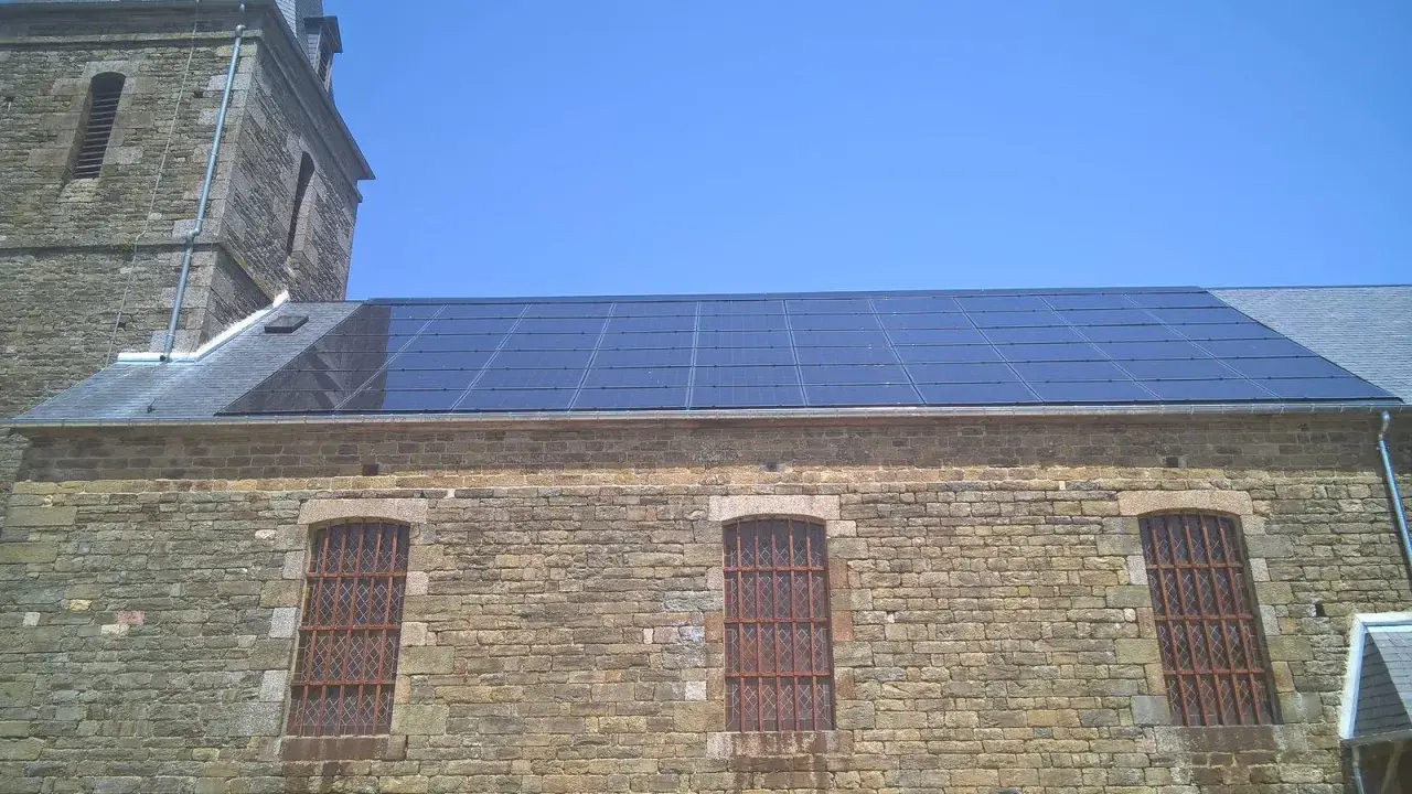 Panneaux solaires installés sur le toit d'un bâtiment en pierre, possiblement dans une zone classée, sous un ciel bleu clair.