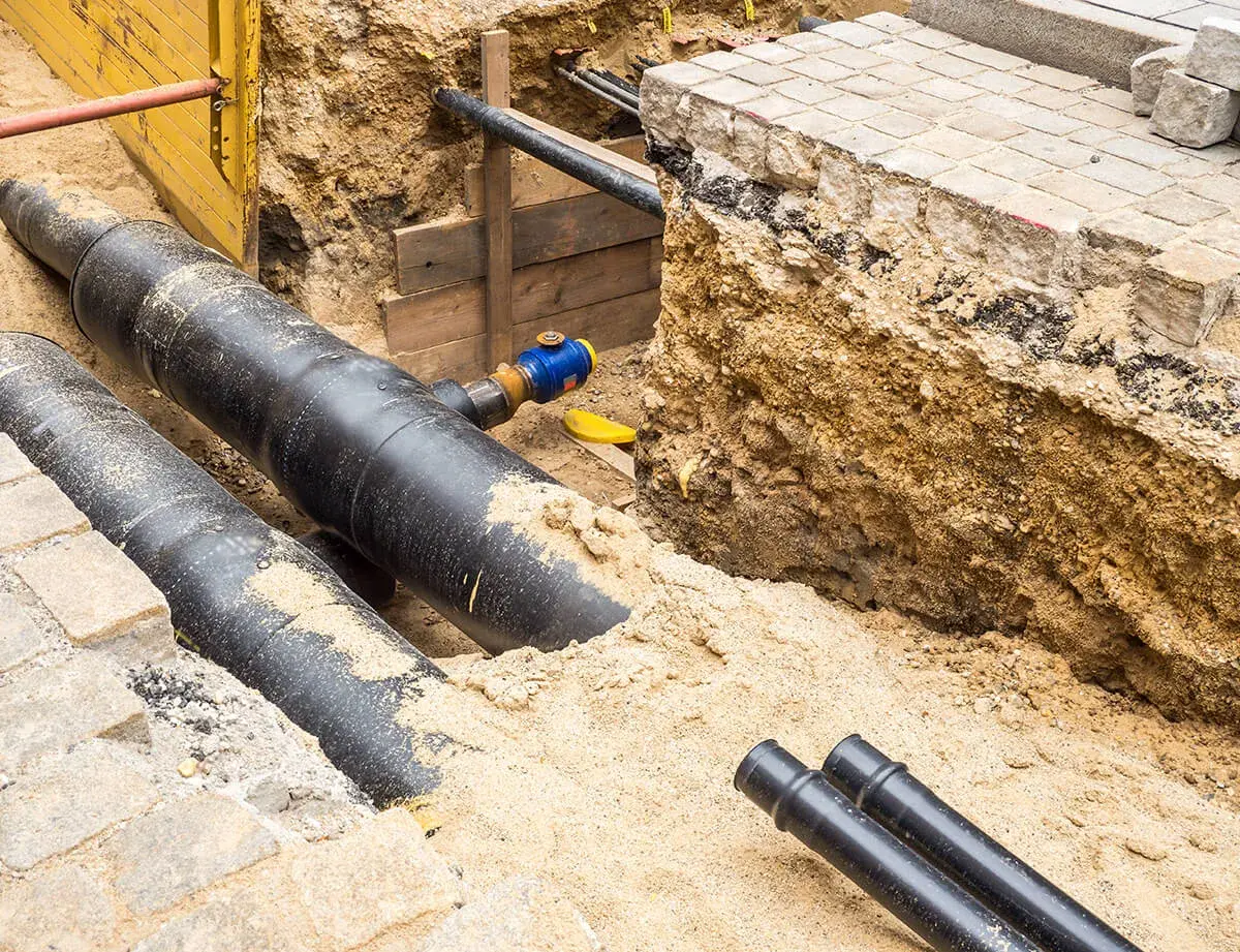 Gros tuyaux noirs enfouis dans le sable, prêts pour le chauffage urbain. Des travaux de voirie en cours.