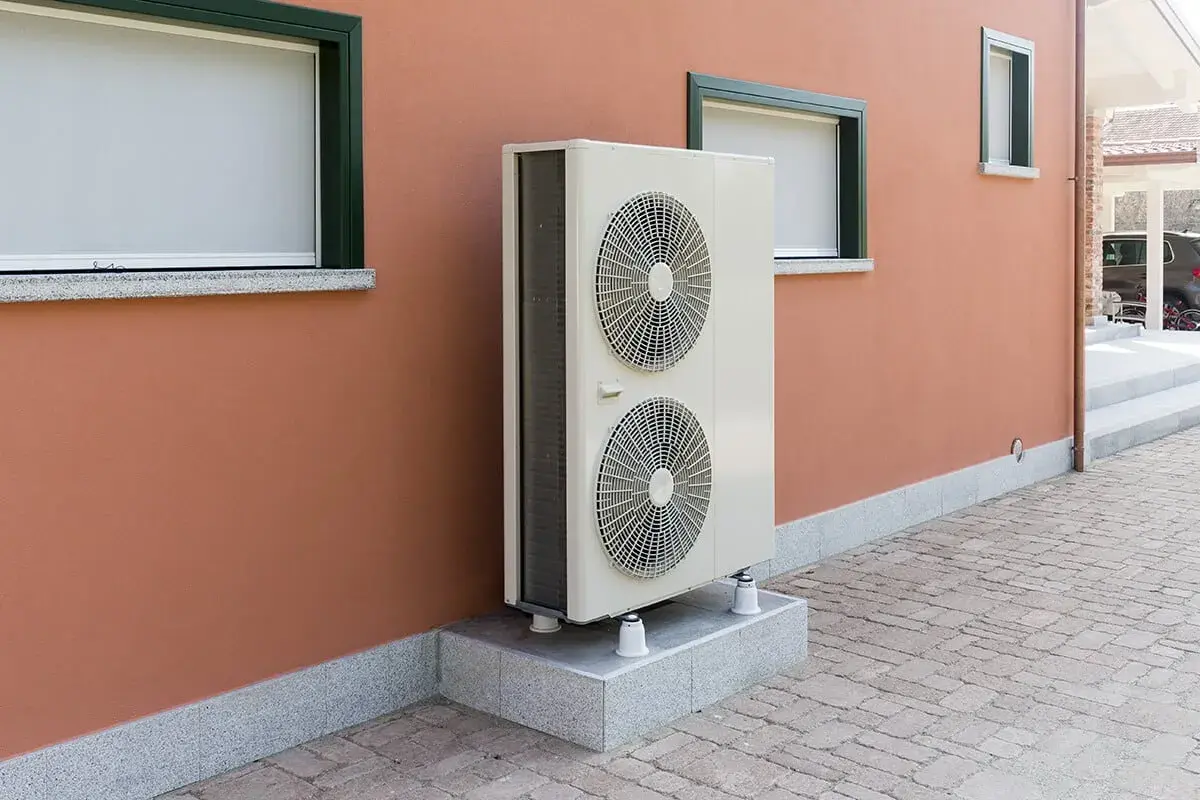 Unité extérieure d'une pompe à chaleur géothermique, installée sur un socle devant un mur ocre. Le prix de ce système est un investissement pour le confort.