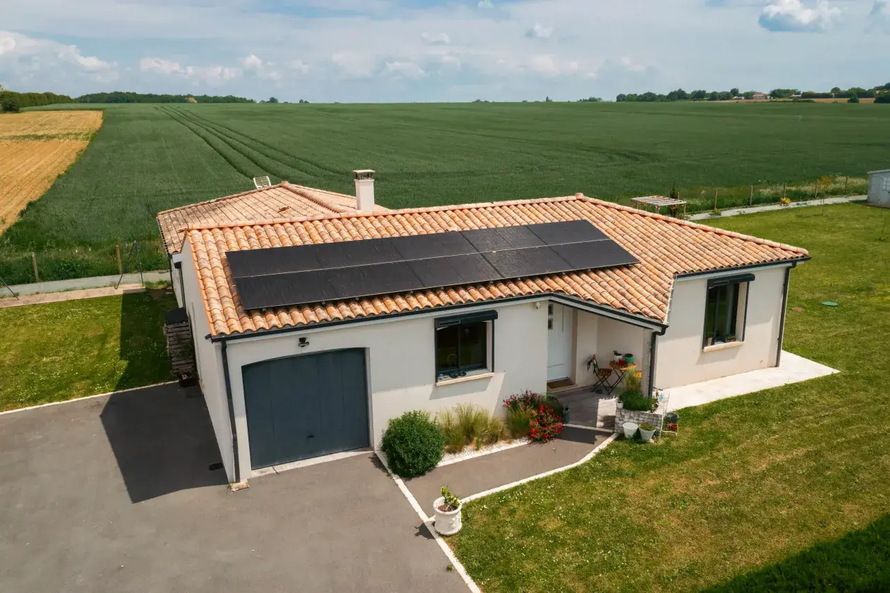 Maison avec toiture photovoltaïque, entourée de verdure et de champs.