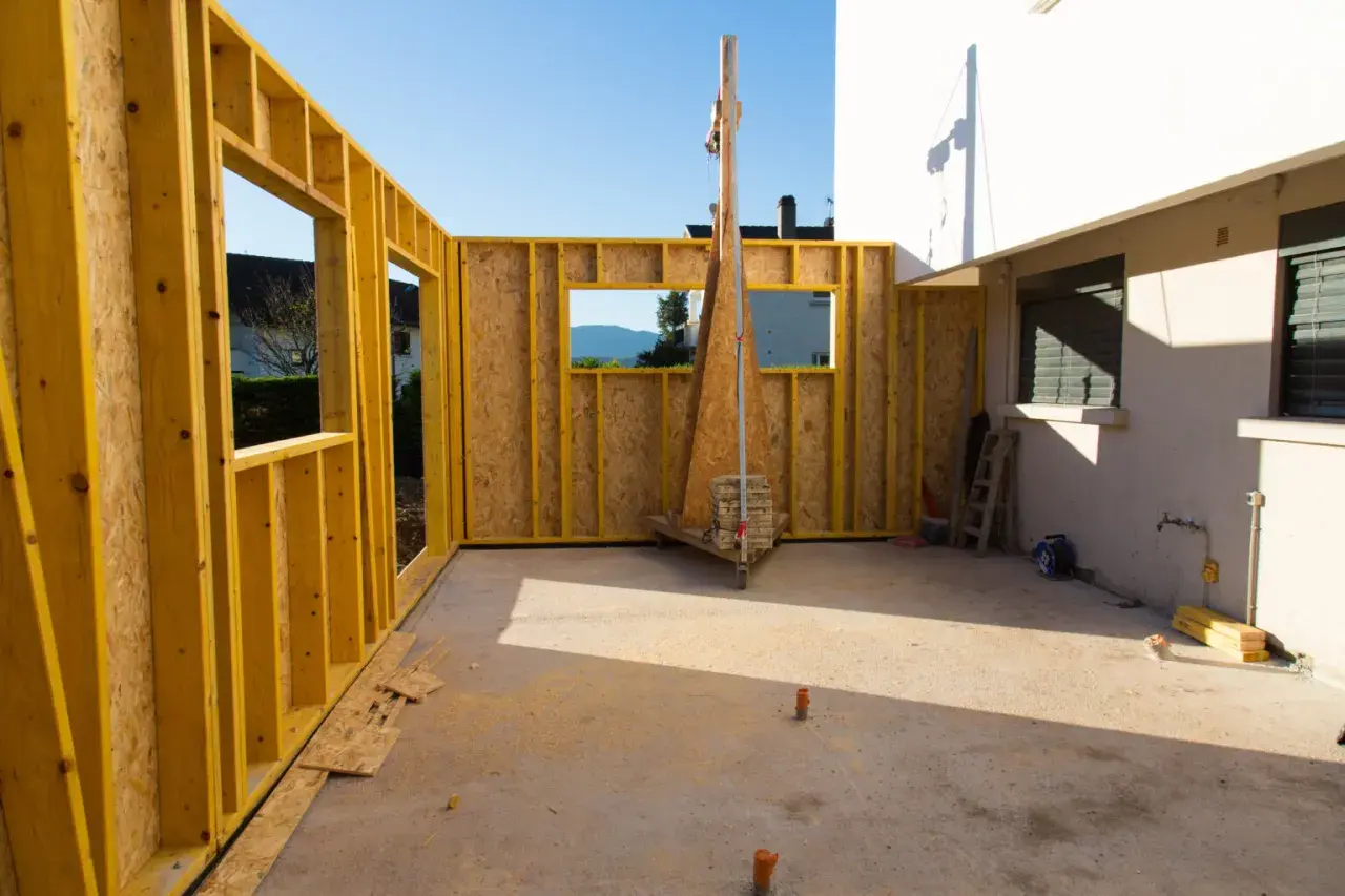 Chantier d'une extension bois, murs en ossature jaune et panneaux OSB, avec vue sur le paysage.