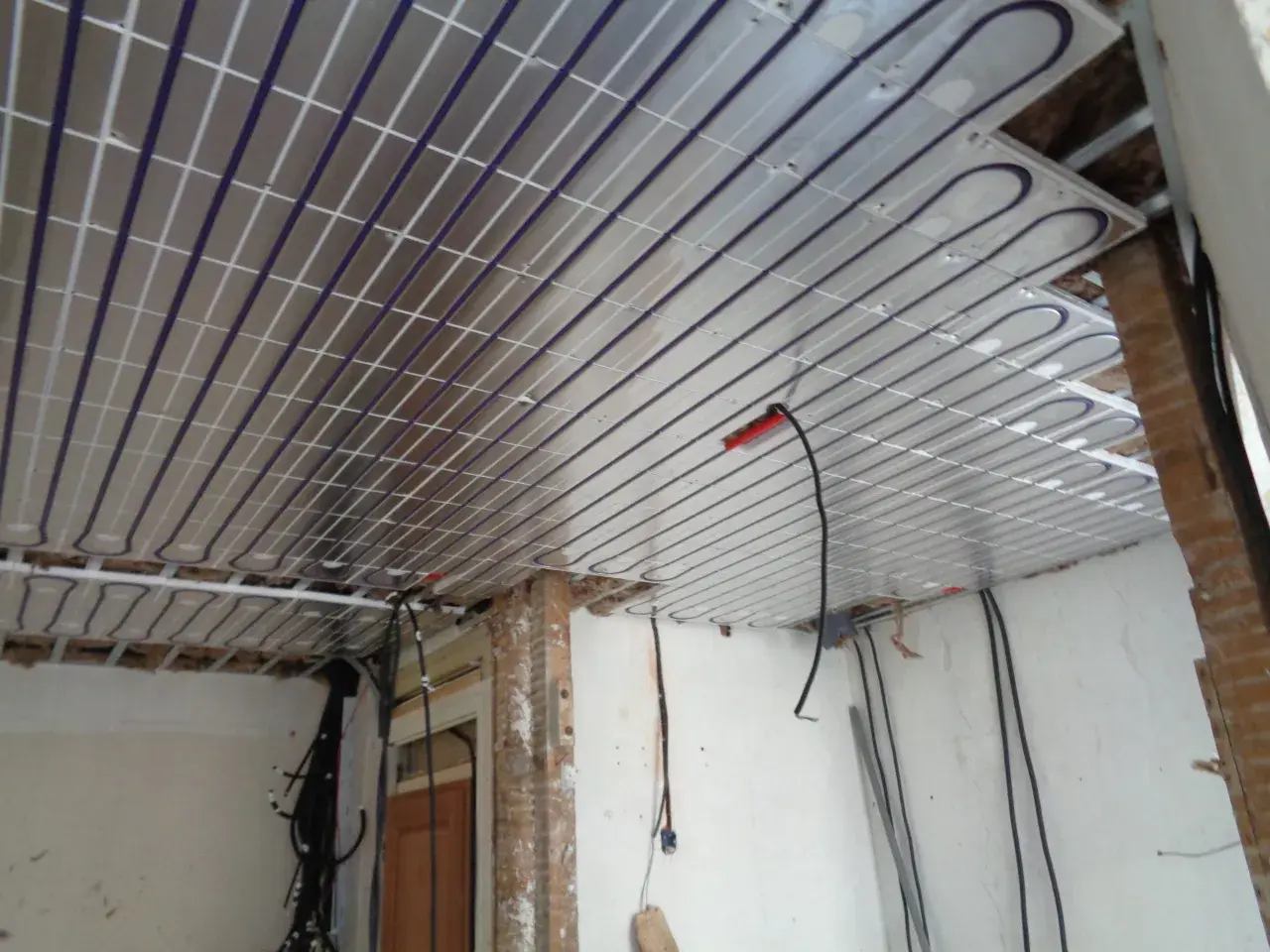 Panneaux de plafond rayonnant installés, prêts pour une chaleur douce et uniforme. Des câbles électriques sont visibles, en attente de connexion.